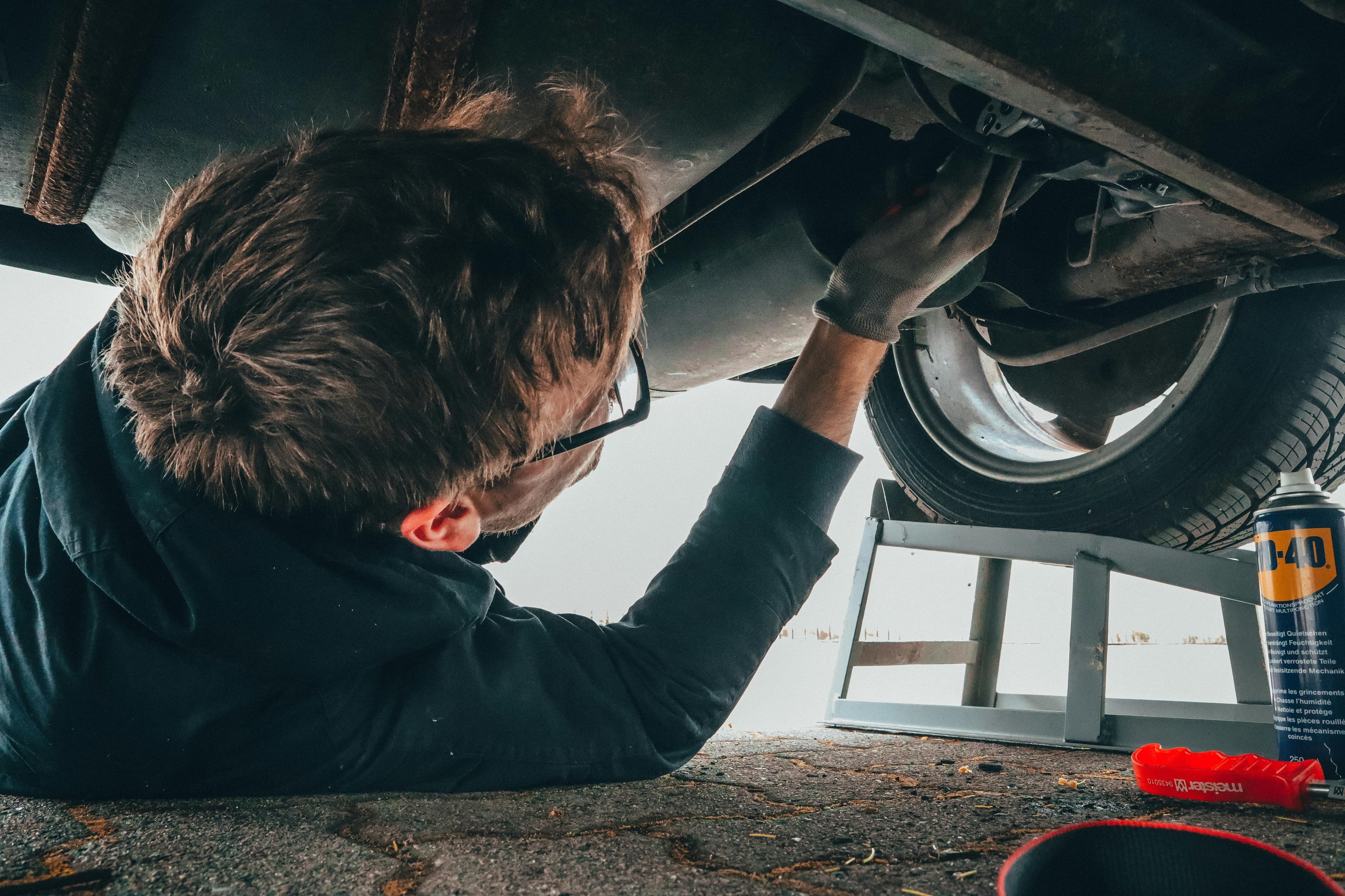 Technician working under a vehicle outdoors with WD-40